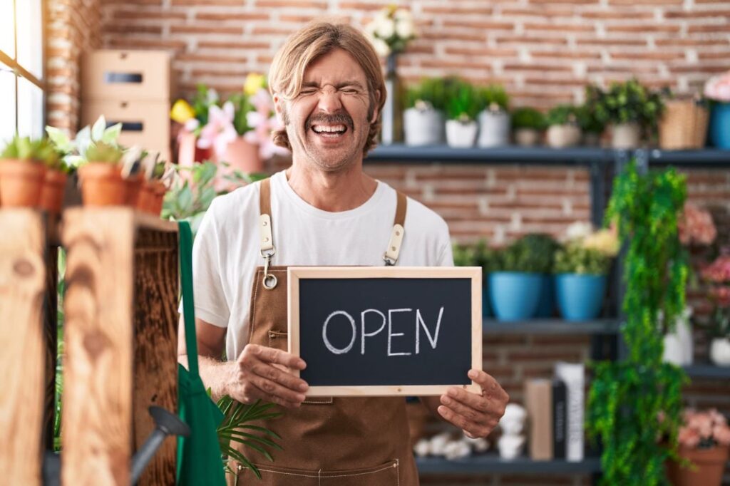 Happy man holding open sign in floral shop