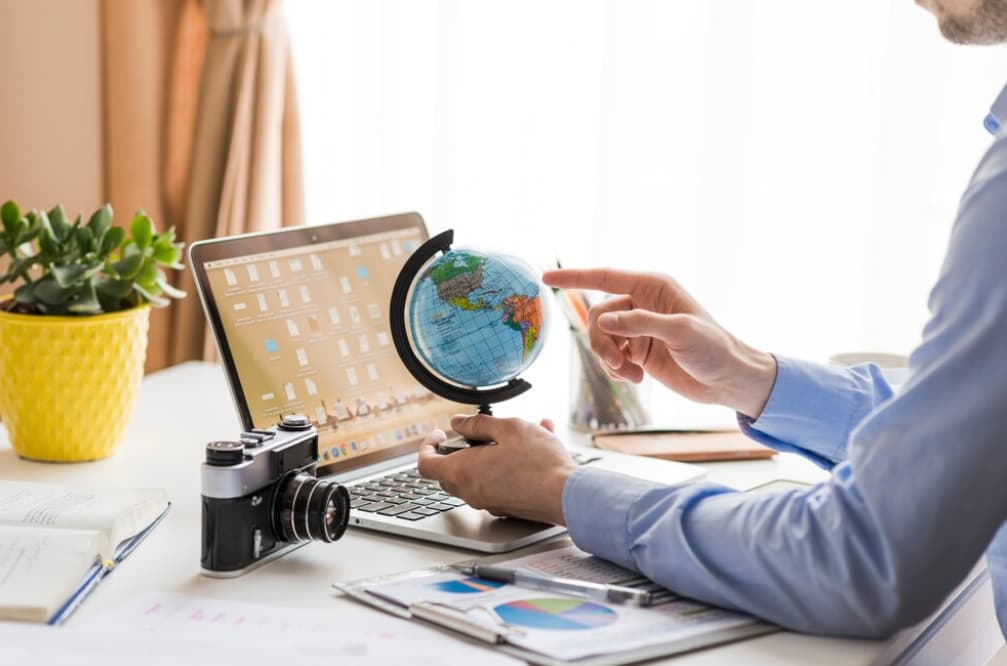 A businessman pointing at a globe beside a laptop and camera